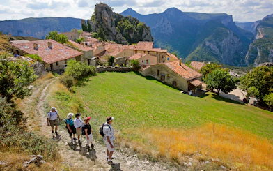 Hikers walking through a village with Gorges du Verdon cliffs in the background.