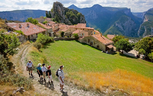 Hikers walking through a village with Gorges du Verdon cliffs in the background.