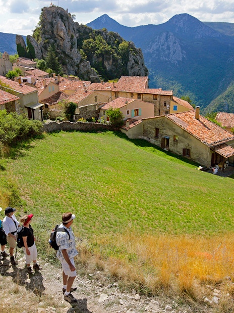 Hikers walking through a village with Gorges du Verdon cliffs in the background.