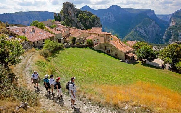 Hikers walking through a village with Gorges du Verdon cliffs in the background.
