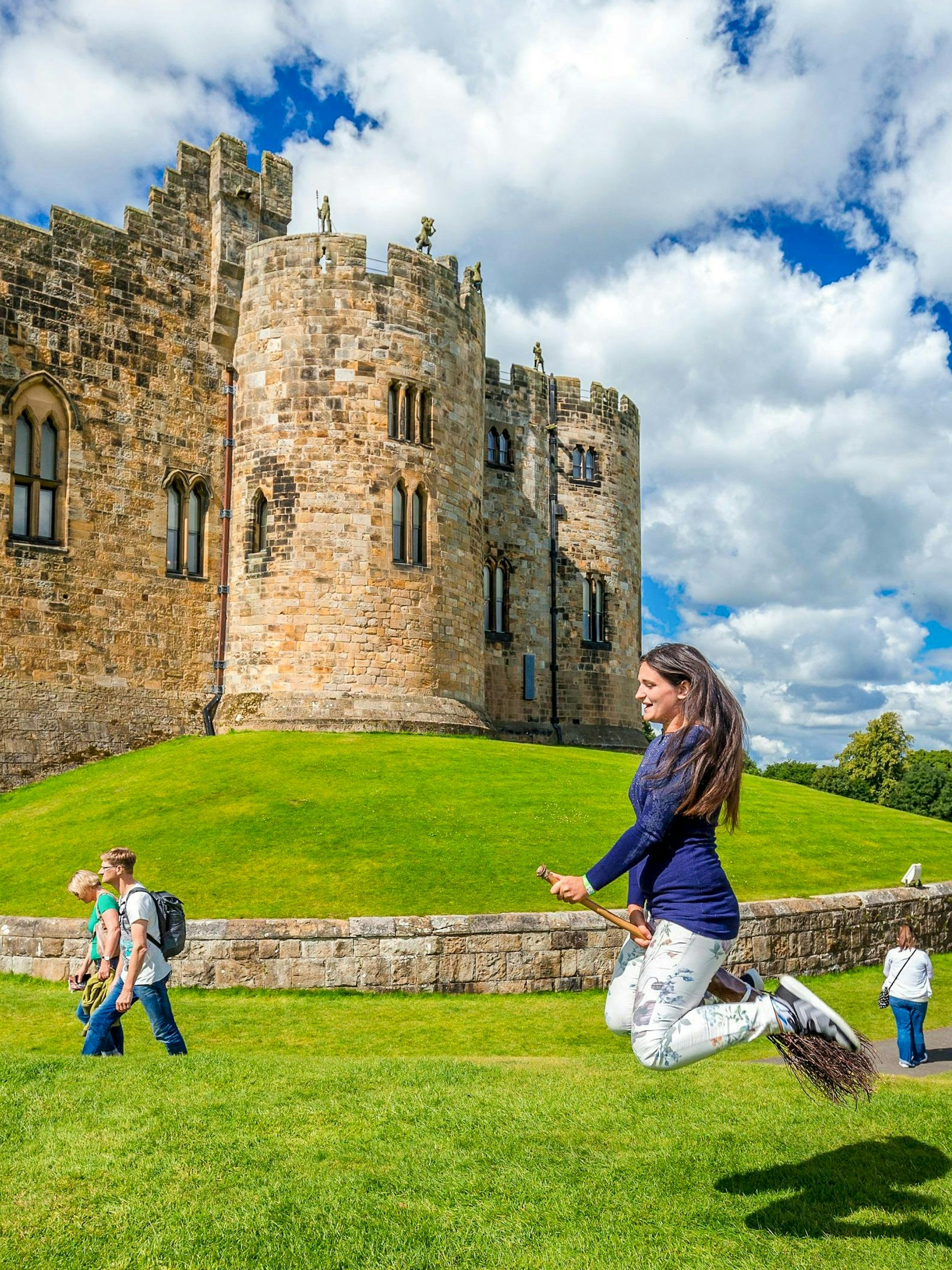 Person on broomstick in front of Alnwick Castle exterior, England.