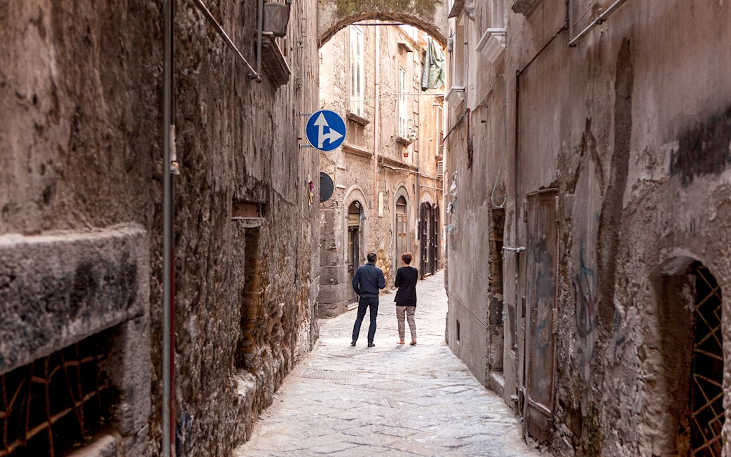 Narrow alleyway in Naples with two people walking under an archway.