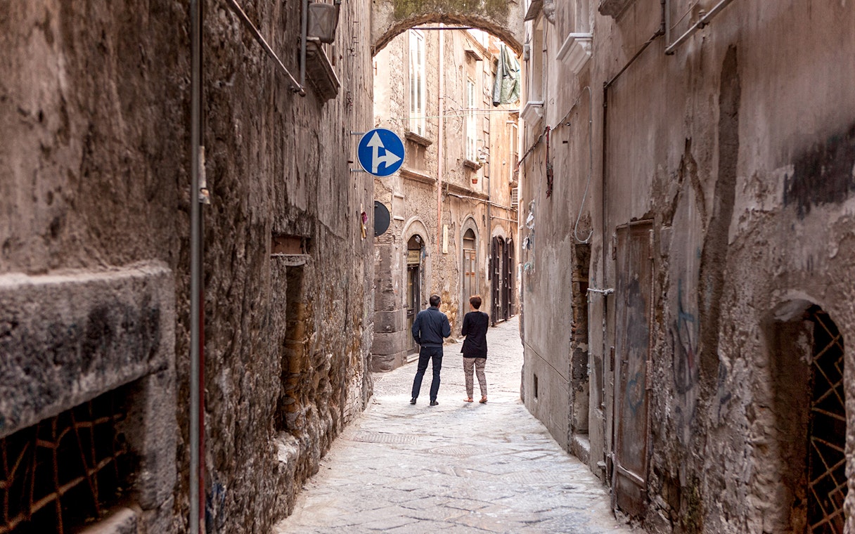 Narrow alleyway in Naples with two people walking under an archway.