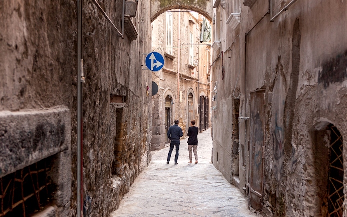 Narrow alleyway in Naples with two people walking under an archway.