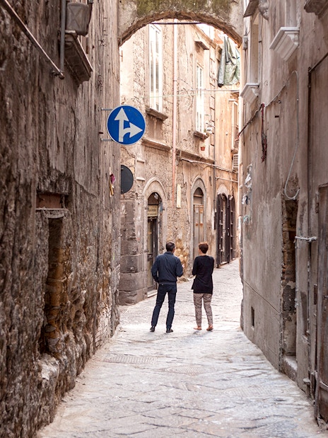 Narrow alleyway in Naples with two people walking under an archway.