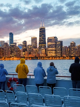People on a boat deck viewing Chicago skyline at dusk with water and cloudy sky.