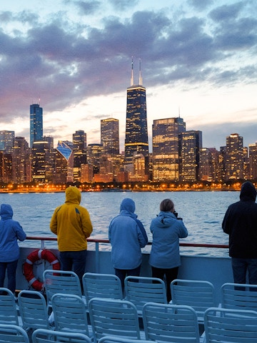 People on a boat deck viewing Chicago skyline at dusk with water and cloudy sky.