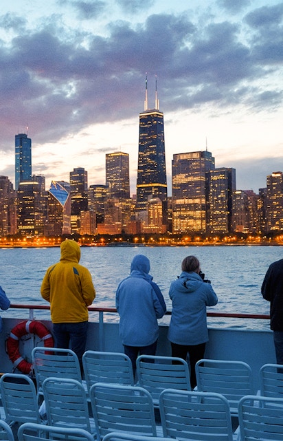 People on a boat deck viewing Chicago skyline at dusk with water and cloudy sky.