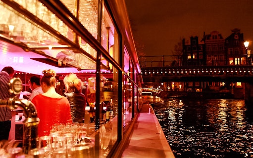Amsterdam canal cruise with illuminated bridges and passengers enjoying the view.