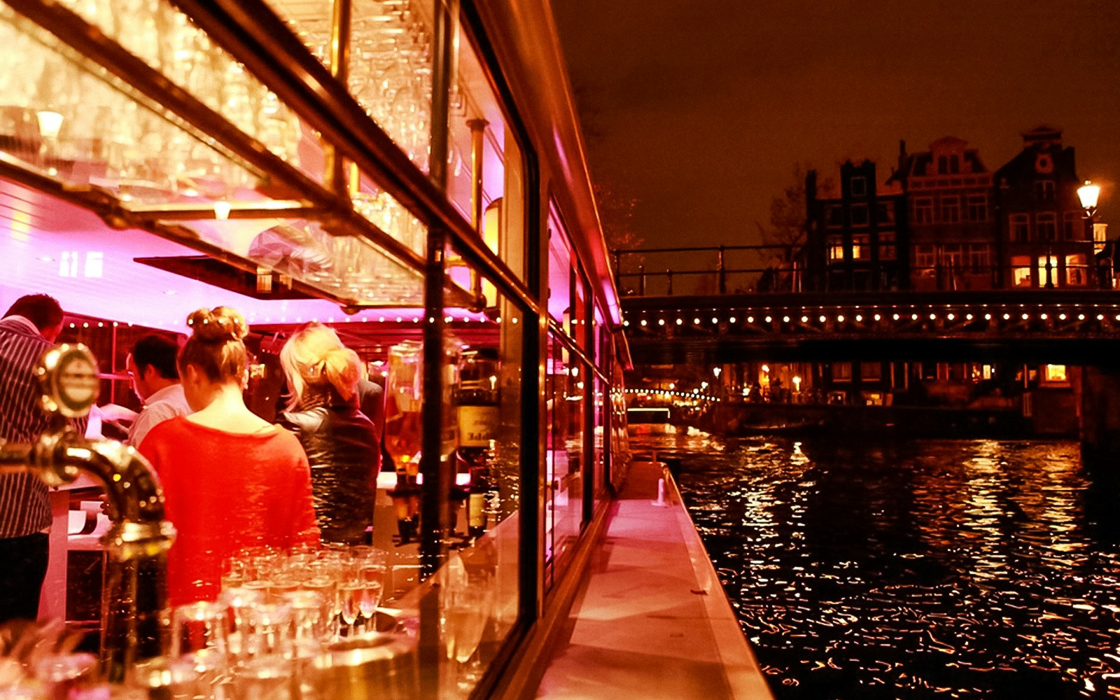 Amsterdam canal cruise with illuminated bridges and passengers enjoying the view.