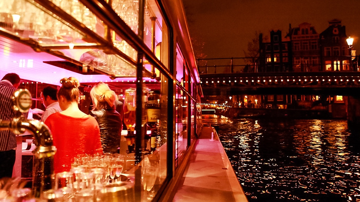 Amsterdam canal cruise with illuminated bridges and passengers enjoying the view.