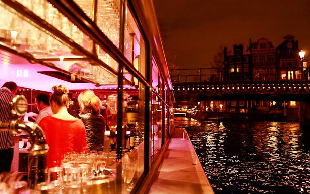 Amsterdam canal cruise with illuminated bridges and passengers enjoying the view.