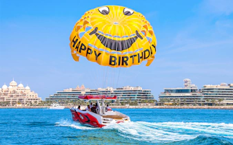 Parasailing over Dubai waters with a smiley parachute and city skyline in the background.