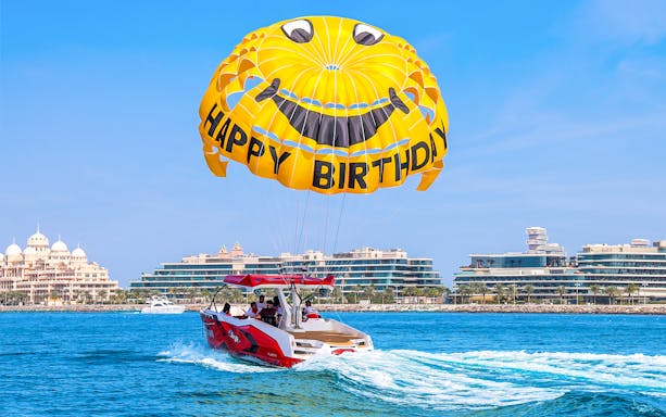Parasailing over Dubai waters with a smiley parachute and city skyline in the background.