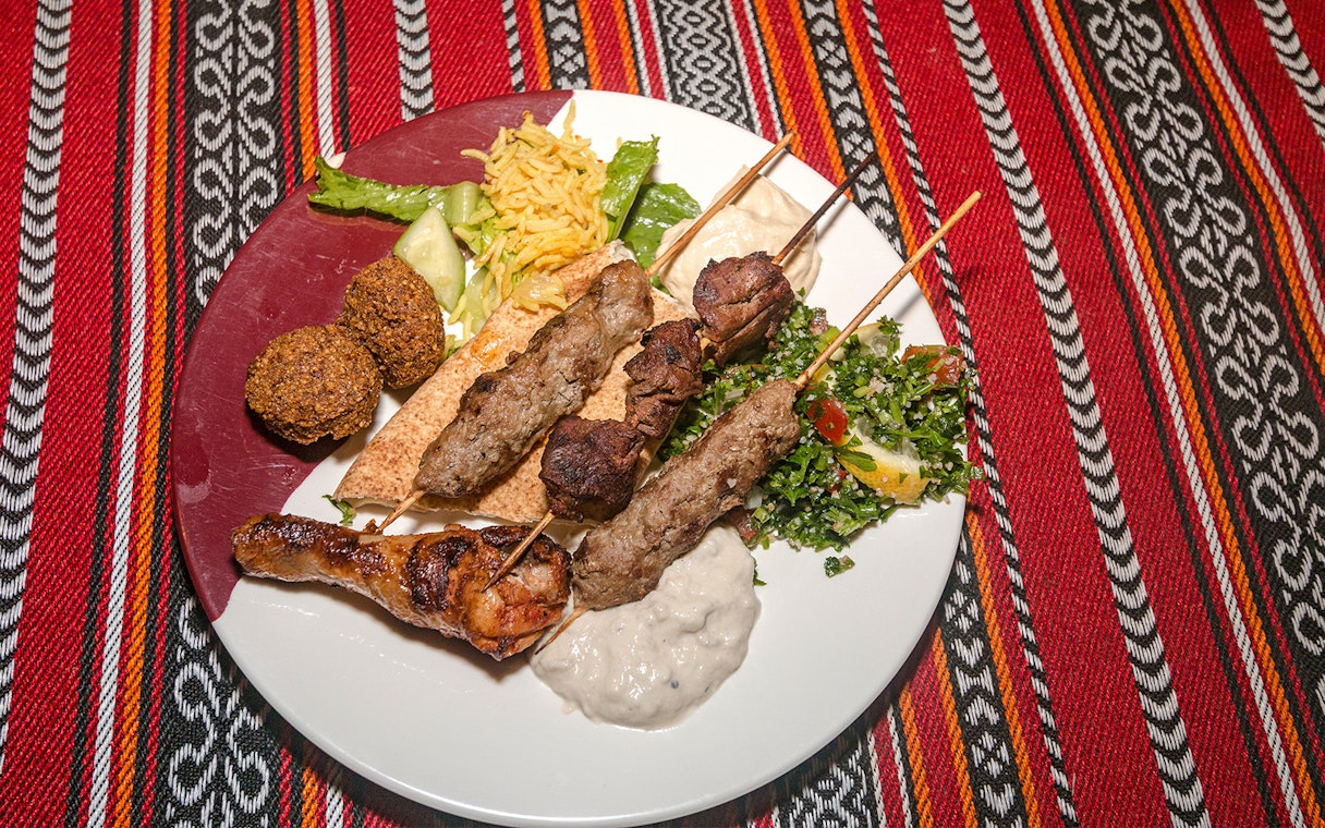 Grilled lamb and beef skewers with chicken, falafel, tabouli, and hummus on a desert safari dinner plate.
