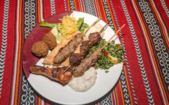 Grilled lamb and beef skewers with chicken, falafel, tabouli, and hummus on a desert safari dinner plate.