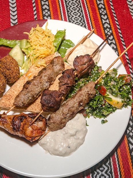 Grilled lamb and beef skewers with chicken, falafel, tabouli, and hummus on a desert safari dinner plate.