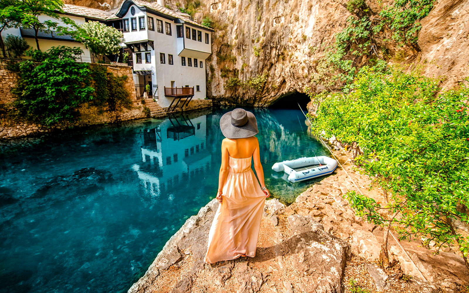 Guest overlooking Blagaj Buna river with historic house and cave in background.