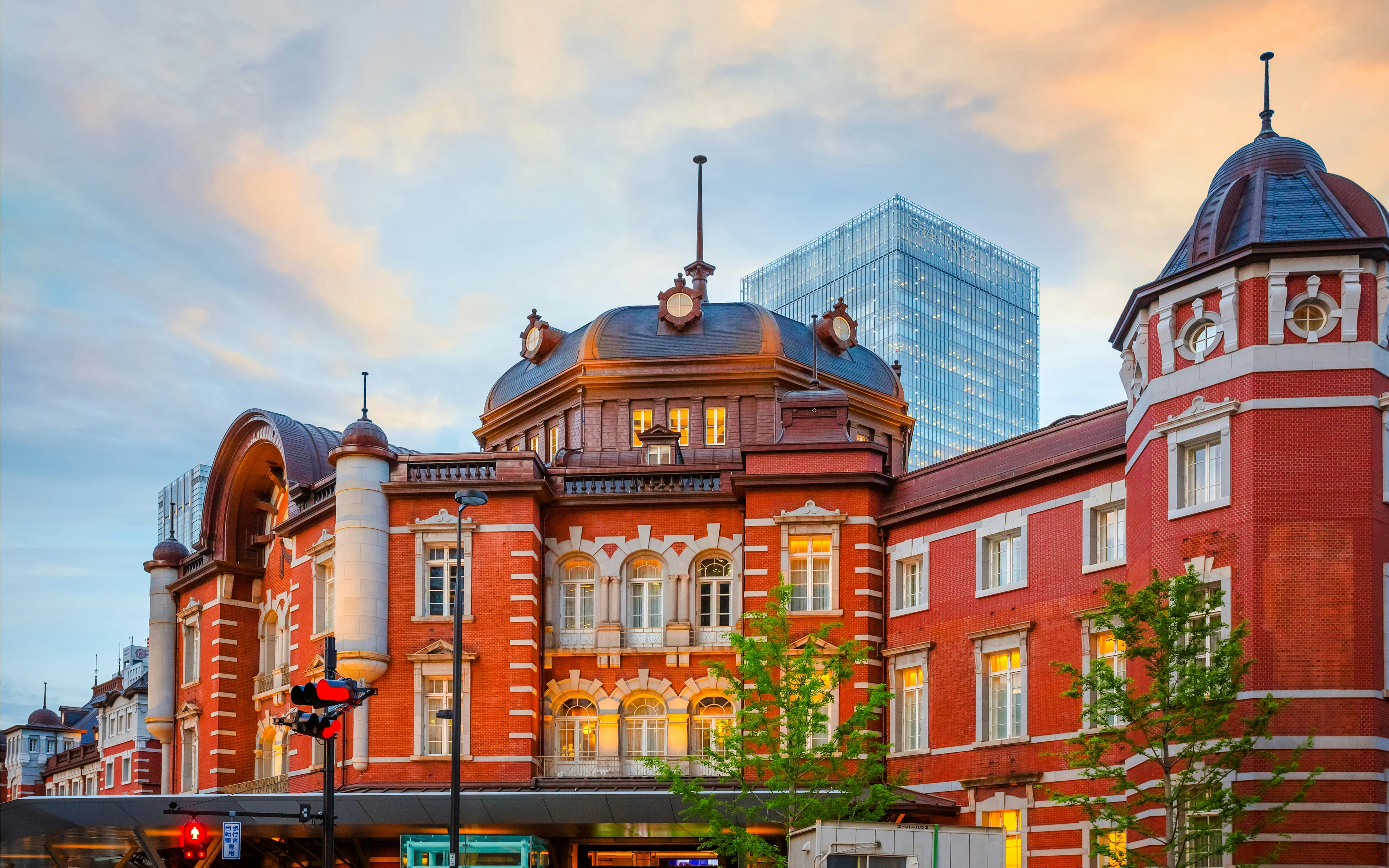 Tokyo Station's red brick facade at dusk with a modern skyscraper in the background.