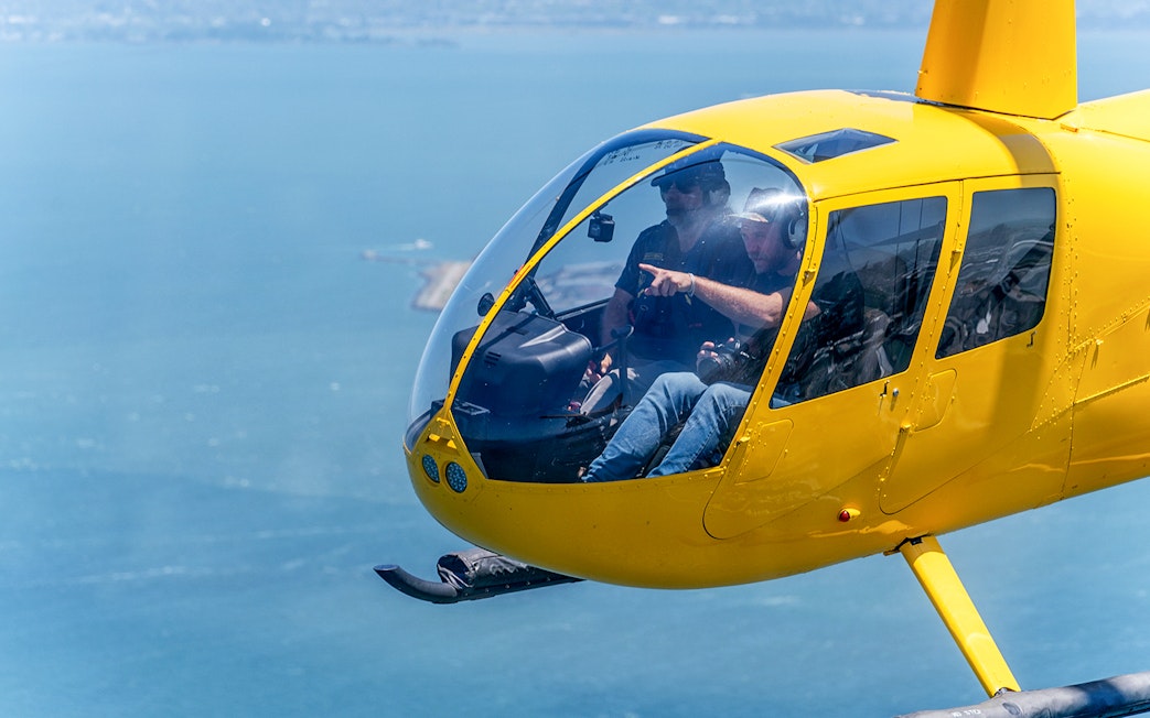 Visitors inside a yellow helicopter flying over a coastal area.
