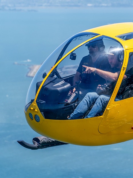 Visitors inside a yellow helicopter flying over a coastal area.