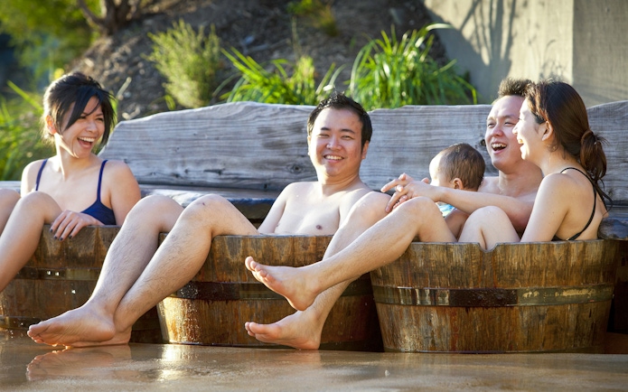 Visitors relaxing in wooden hot tubs at Peninsula Hot Springs, enjoying a spa day experience.