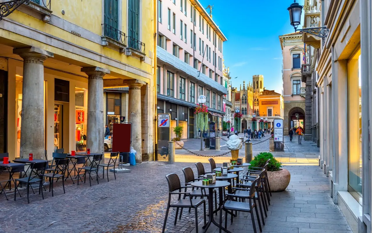 Outdoor café seating along a cobblestone street in Padua, Italy, with historic buildings in the background.