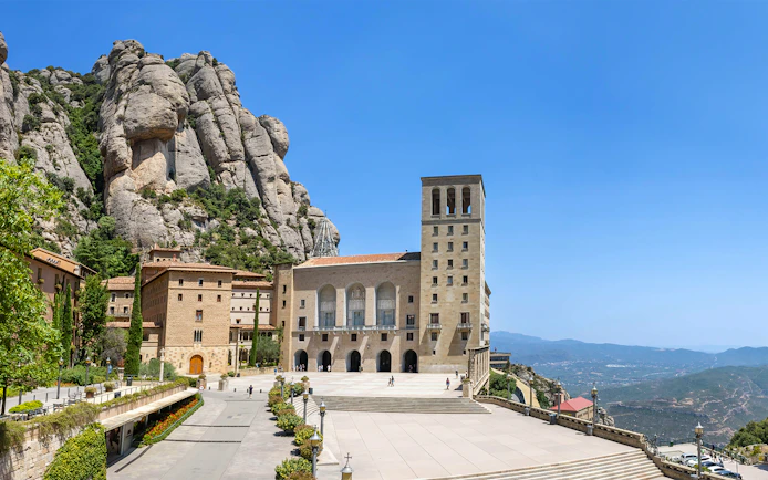 Abbey of Montserrat with mountain backdrop and courtyard in Catalonia, Spain.