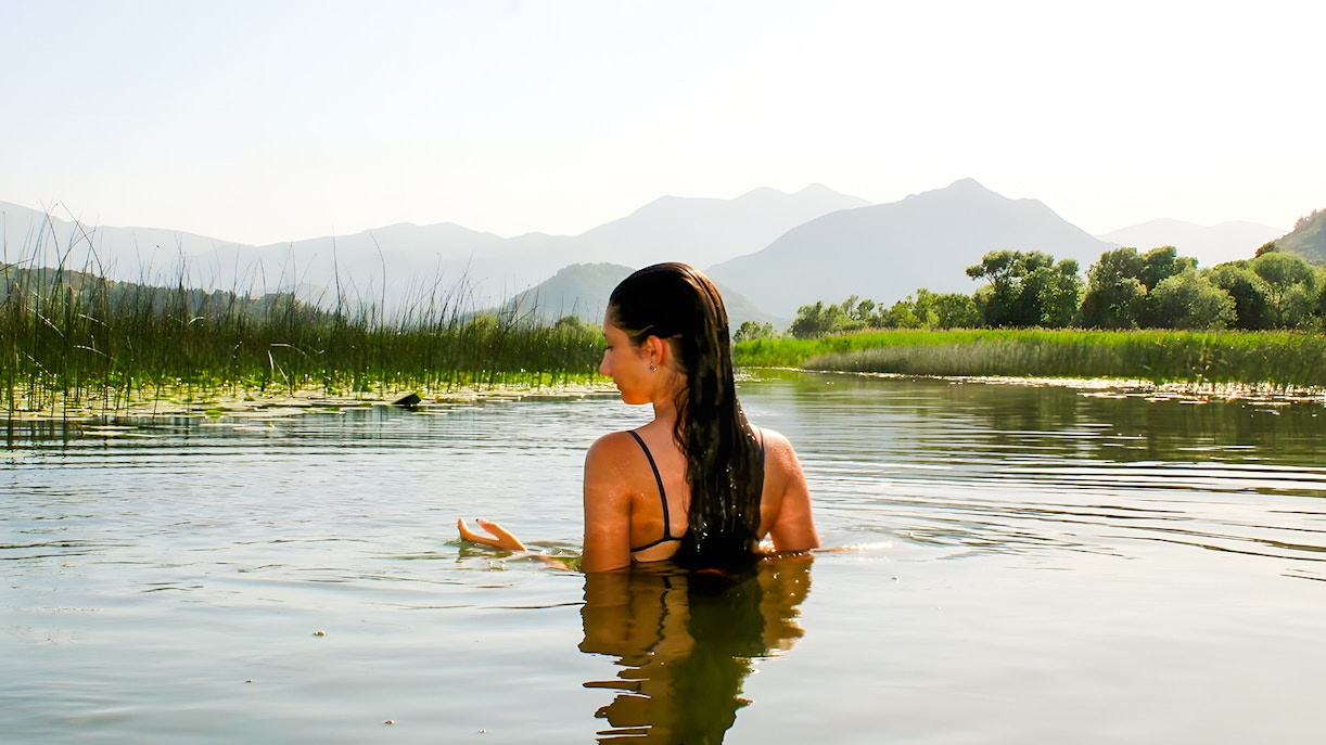 Woman swimming in Lake Skadar with mountains in the background.