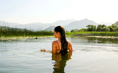 Woman swimming in Lake Skadar with mountains in the background.