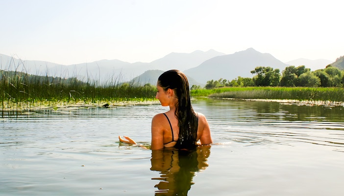 Woman swimming in Lake Skadar with mountains in the background.