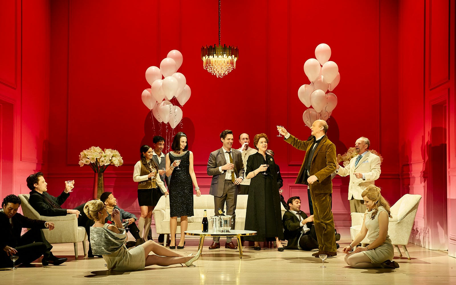 Group of people in formal attire celebrating with drinks and balloons in a red room.