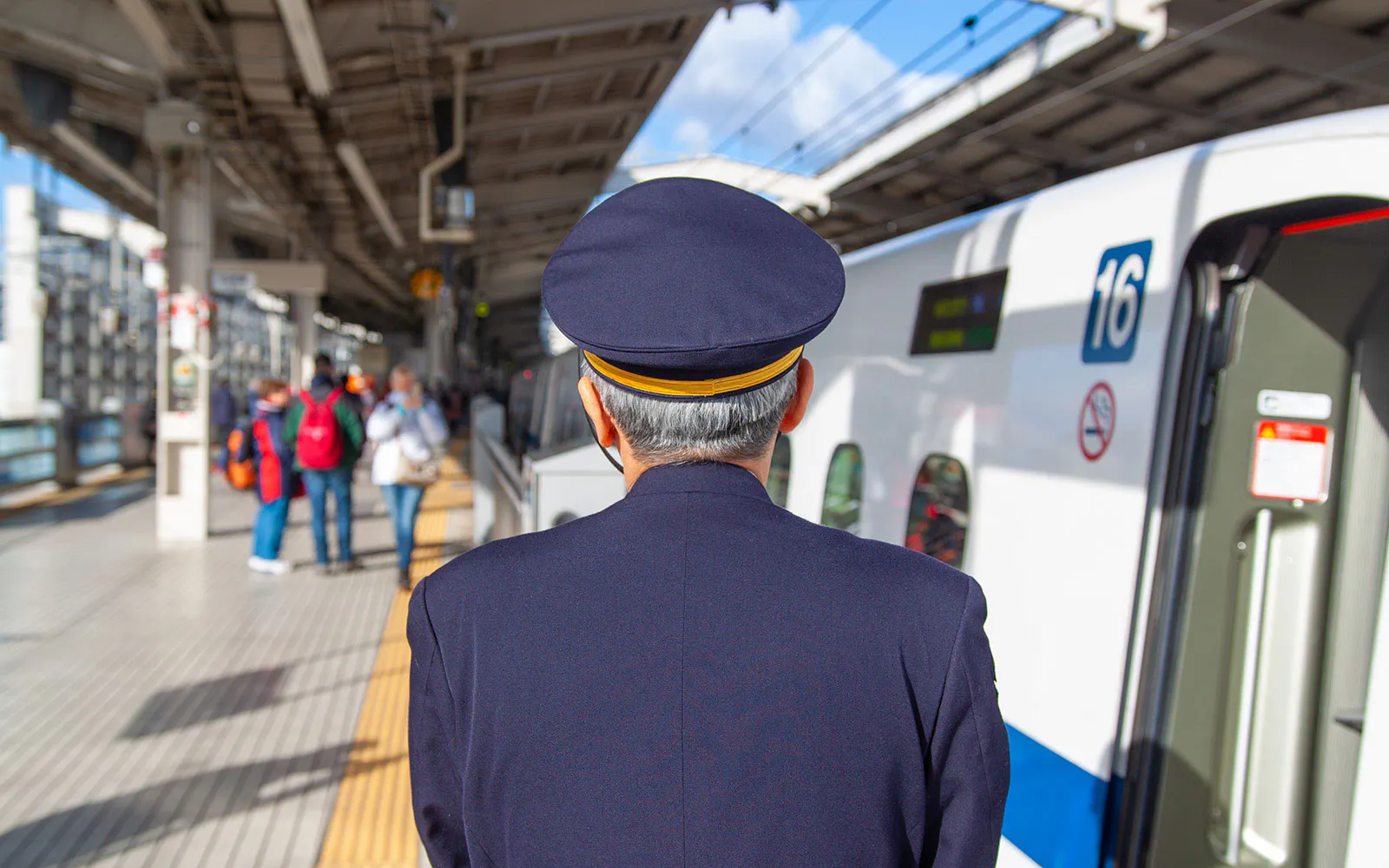 Conductor checks platform beside Shinkansen Nozomi train in Japan.