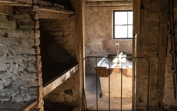 Prison cell interior in Auschwitz Block 11 with wooden bunks and barred window.