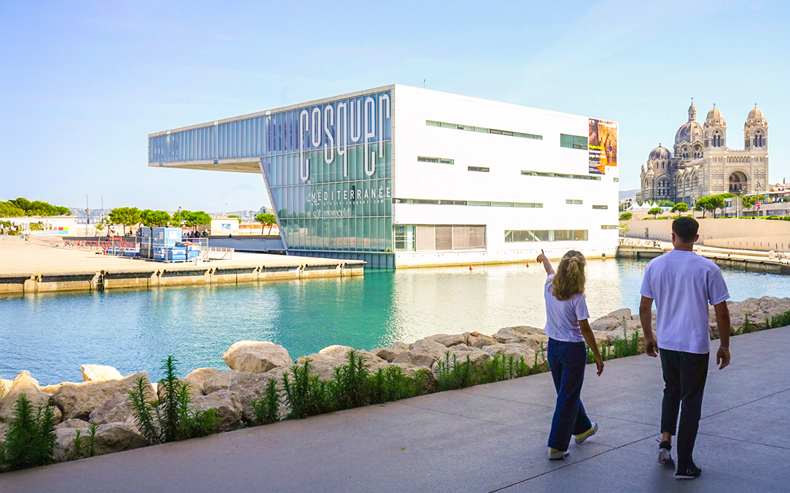 Cosquer Cave building in Marseille with people walking nearby, cathedral in background.
