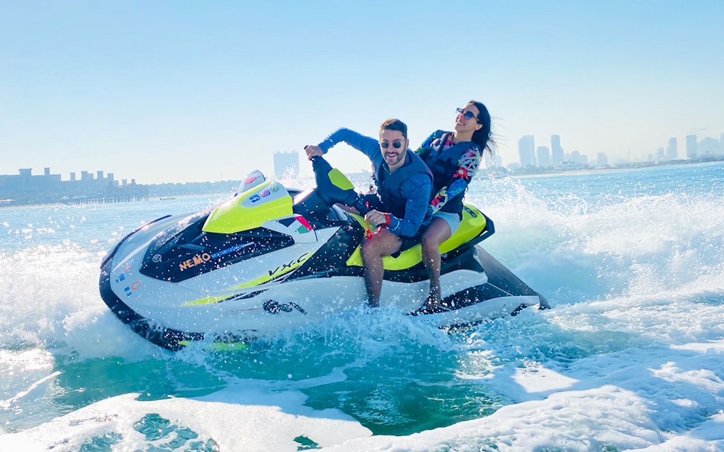 Tourists riding a jet ski in Dubai with city skyline in the background.