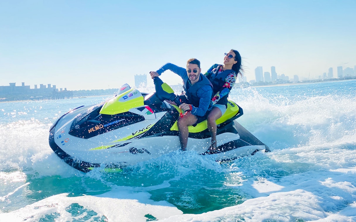 Tourists riding a jet ski in Dubai with city skyline in the background.