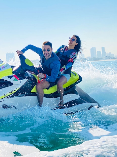 Tourists riding a jet ski in Dubai with city skyline in the background.