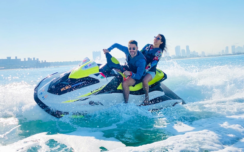 Tourists riding a jet ski in Dubai with city skyline in the background.