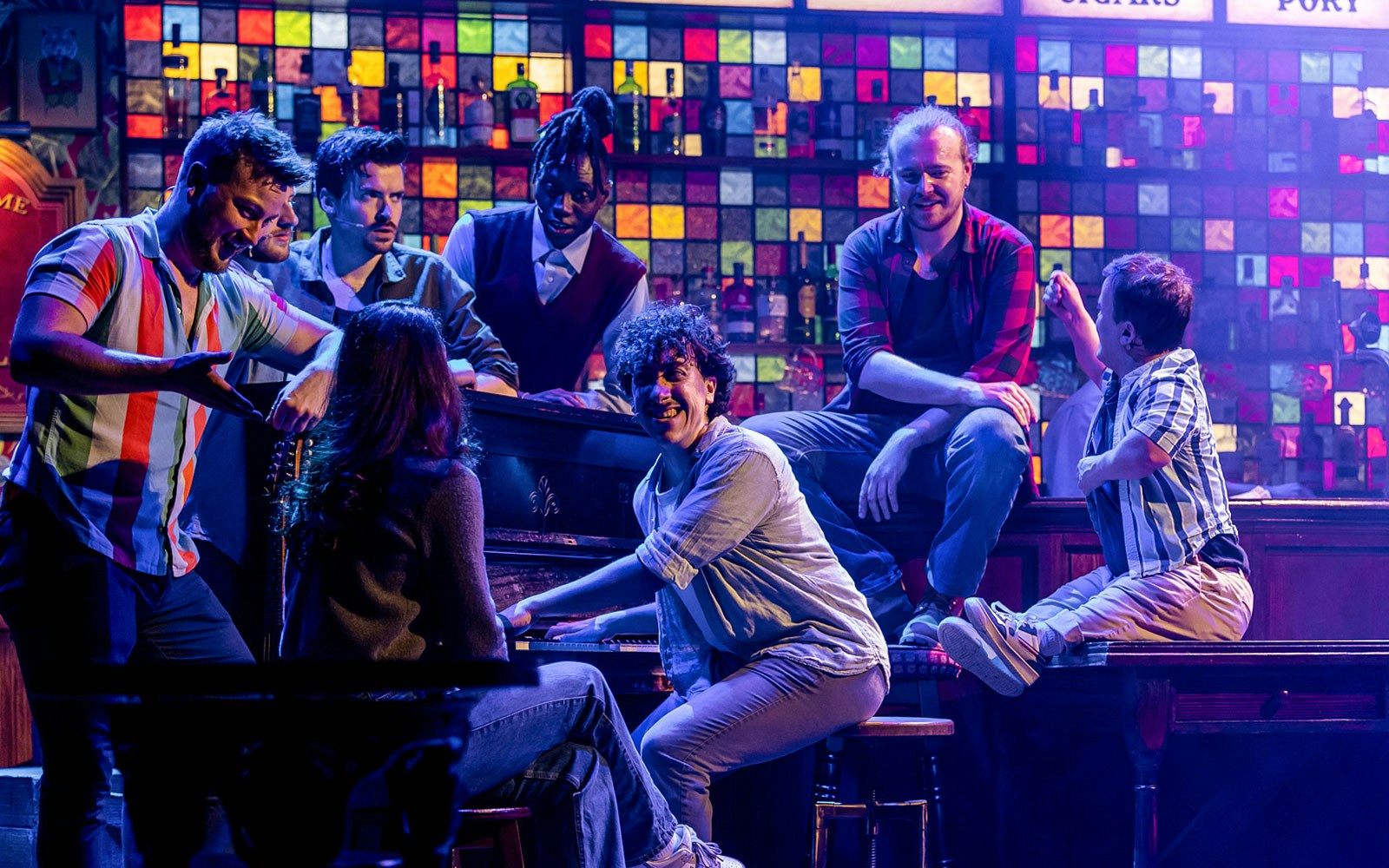 Performers from The Choir of Man show gathered around a piano on stage.