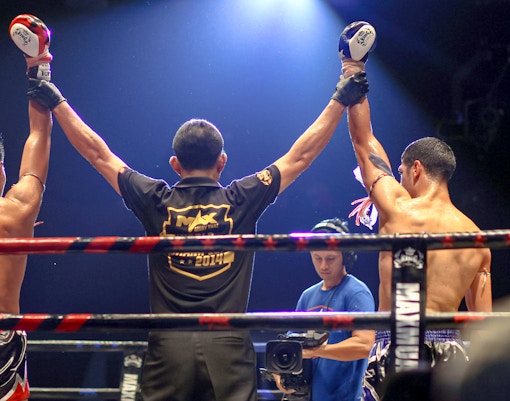 Referee raises fighters' arms in Max Muay Thai boxing ring.