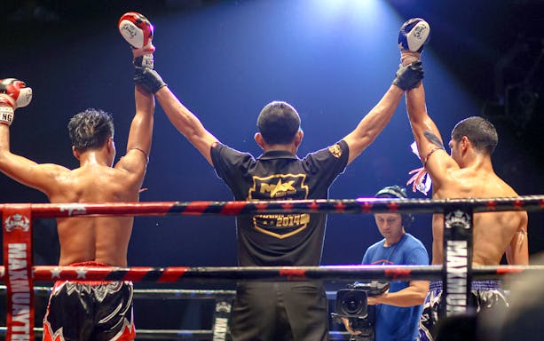 Referee raises fighters' arms in Max Muay Thai boxing ring.