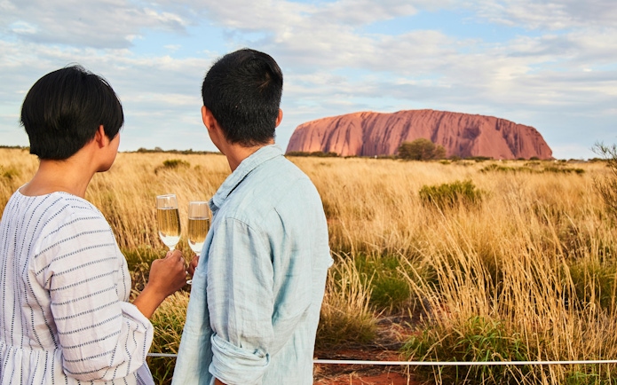 Couple enjoying champagne with view of Uluru at sunset, Australia.