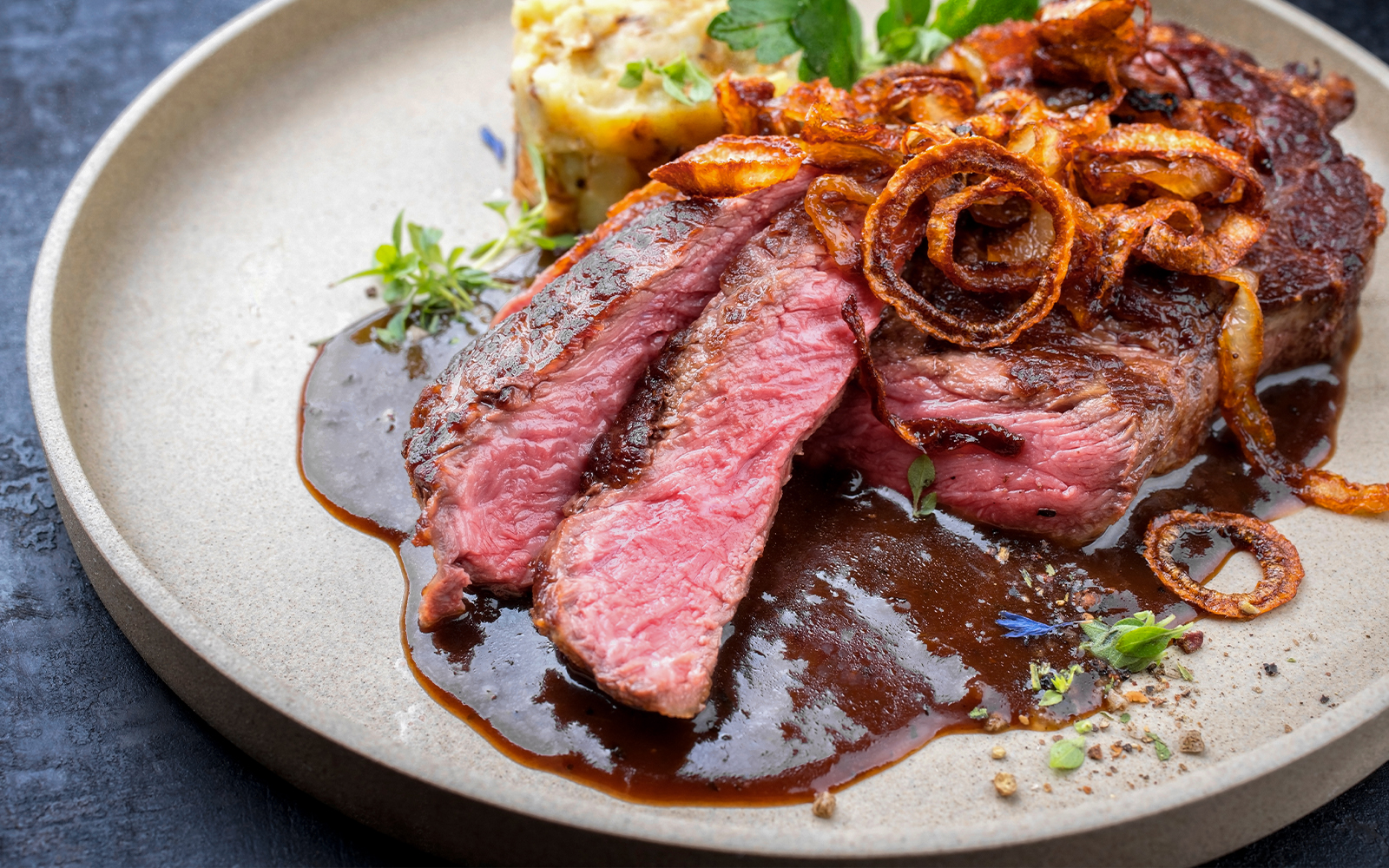 Grilled steak with sauce and crispy onions on a plate.