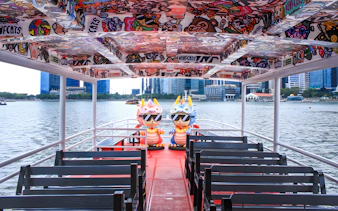 Colorful interior of a Singapore River Cruise boat by WaterB with city skyline in the background.