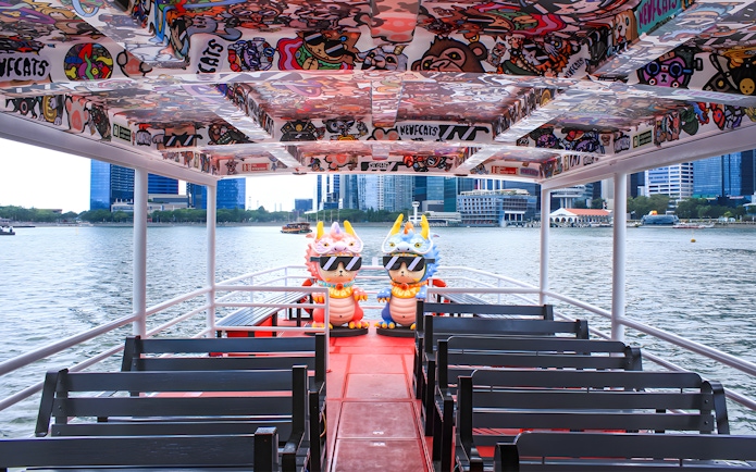 Colorful interior of a Singapore River Cruise boat by WaterB with city skyline in the background.