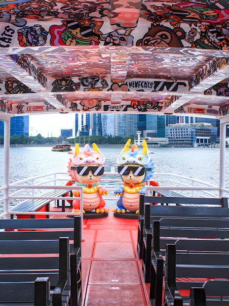 Colorful interior of a Singapore River Cruise boat by WaterB with city skyline in the background.