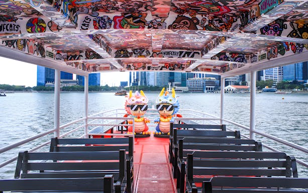 Colorful interior of a Singapore River Cruise boat by WaterB with city skyline in the background.