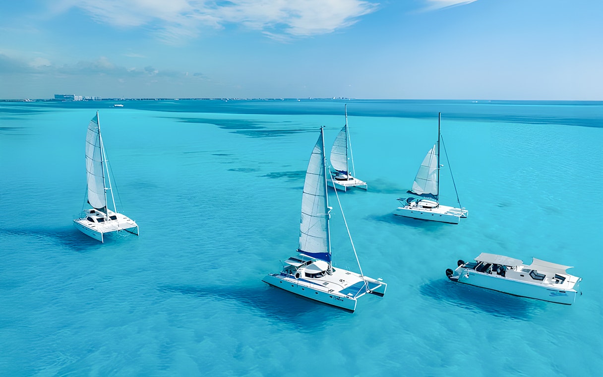 Catamarans sailing in turquoise Caribbean Sea near Cancún, Mexico coastline.