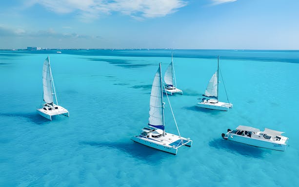 Catamarans sailing in turquoise Caribbean Sea near Cancún, Mexico coastline.